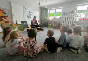 Dzieci siedzą na dywanie i słuchają informacji o mrówkach
