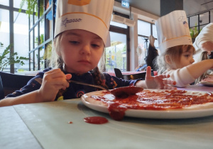 Dziewczynka smaruje swoją pizzę sosem pomidorowym