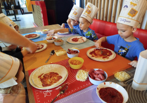 Dzieci komponują swoją pizzę - układają na cieście wybrane przez siebie składniki