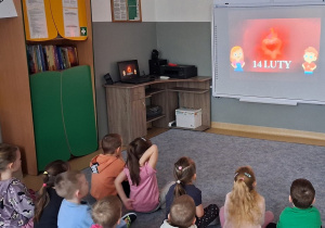 Dzieci siedzą na dywanie i oglądają film edukacyjny na temat Walentynek