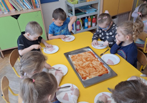 Dzieci na talerzykach kroją szynkę na kawałeczki