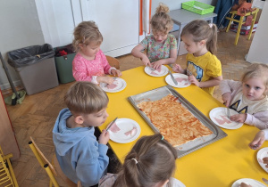 Dzieci na talerzykach kroją szynkę na kawałeczki