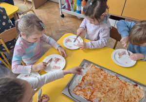Dzieci na talerzykach kroją szynkę na kawałeczki