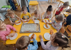 Dzieci jedzą przygotowaną przez siebie pizzę