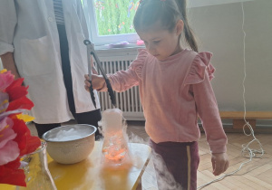 Prowadząca wykonuje eksperymenty z suchym lodem, powiada o nich dzieciom i angażuje dzieci do części zabaw z suchym lodem