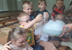 Prowadząca wykonuje eksperymenty z suchym lodem, powiada o nich dzieciom i angażuje dzieci do części zabaw z suchym lodem