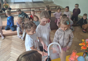 Prowadząca wykonuje eksperymenty z suchym lodem, powiada o nich dzieciom i angażuje dzieci do części zabaw z suchym lodem
