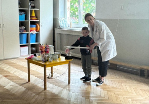 Prowadząca wykonuje eksperymenty z suchym lodem, powiada o nich dzieciom i angażuje dzieci do części zabaw z suchym lodem
