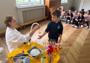 Prowadząca wykonuje eksperymenty z suchym lodem, powiada o nich dzieciom i angażuje dzieci do części zabaw z suchym lodem