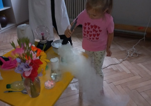 Prowadząca wykonuje eksperymenty z suchym lodem, powiada o nich dzieciom i angażuje dzieci do części zabaw z suchym lodem