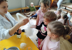 Prowadząca wykonuje eksperymenty z suchym lodem, powiada o nich dzieciom i angażuje dzieci do części zabaw z suchym lodem