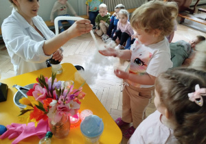 Prowadząca wykonuje eksperymenty z suchym lodem, powiada o nich dzieciom i angażuje dzieci do części zabaw z suchym lodem